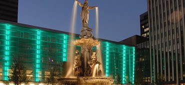 A fountain with lights and statues in front of it.