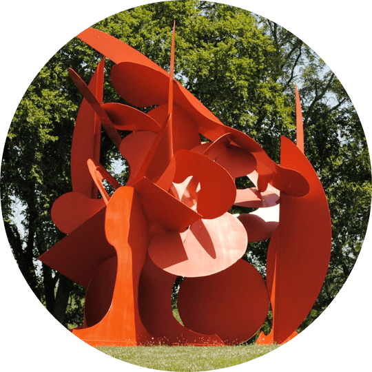 A red sculpture in the grass near trees.